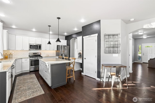 10713 Palisades St SE, Yelm, WA 98597 - kitchen with stainless steel appliances, arched walkways, a sink, decorative backsplash, and light stone counters