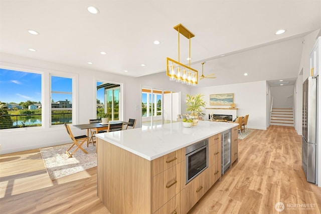 5425 Salish Rd, Blaine, WA 98230 - kitchen featuring modern cabinets, light brown cabinetry, appliances with stainless steel finishes, a warm lit fireplace, and light wood-style flooring