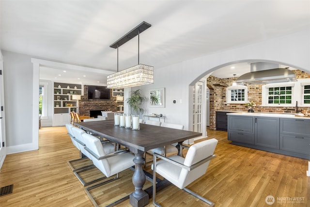 1542 Grand Ave, Seattle, WA 98122 - dining room with arched walkways, light wood-type flooring, brick wall, a brick fireplace, and baseboards