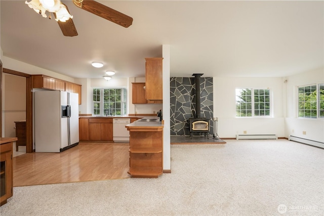 818 295th St E, Roy, WA 98580 - kitchen featuring white appliances, light carpet, a wood stove, ceiling fan, and brown cabinetry