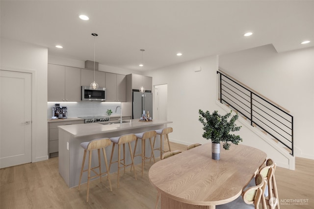 9223A 14th Ave NW, Seattle, WA 98117 - kitchen featuring appliances with stainless steel finishes, a kitchen breakfast bar, an island with sink, light wood finished floors, and a sink