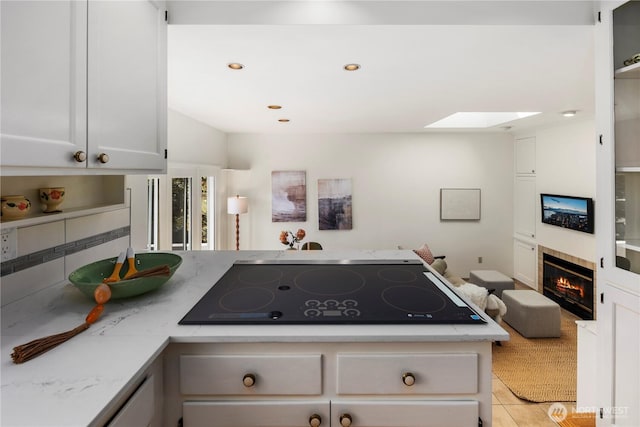 3249 Conkling Pl W, Seattle, WA 98119 - kitchen featuring a skylight, black electric cooktop, a fireplace, light stone counters, and light tile patterned flooring
