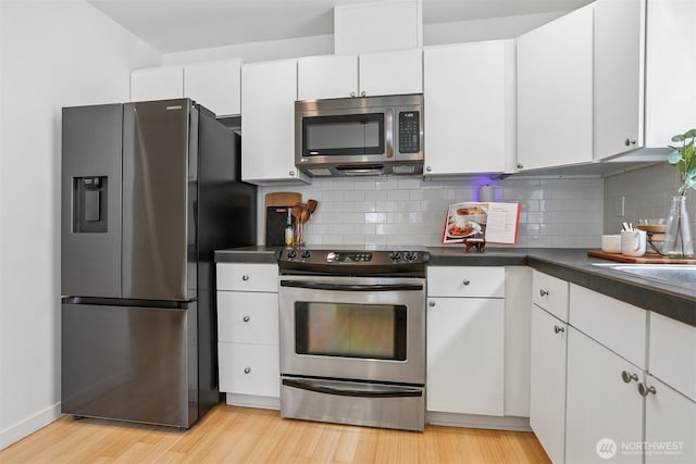 5028 Delridge Way SW Unit C, Seattle, WA 98106 - kitchen featuring appliances with stainless steel finishes, light wood-style floors, dark countertops, white cabinets, and decorative backsplash