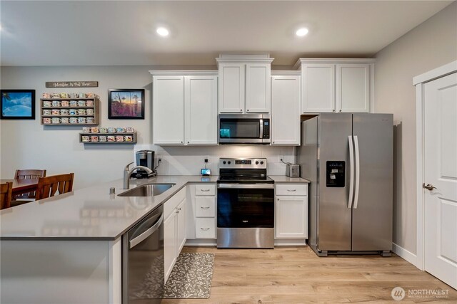 8323 E Gilman Ave, Arlington, WA 98223 - kitchen with appliances with stainless steel finishes, a sink, a peninsula, light wood finished floors, and white cabinetry