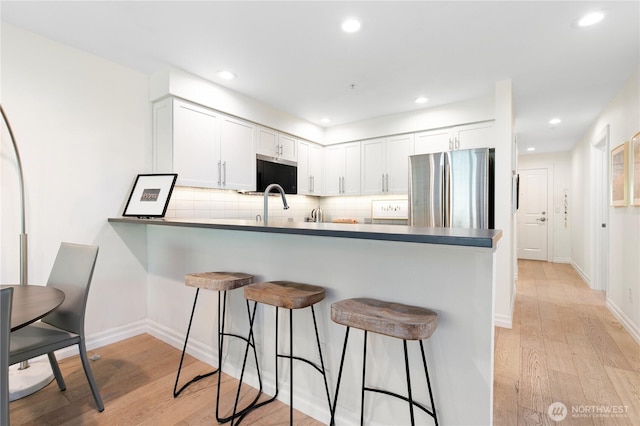 215 20th Ave E Unit 203, Seattle, WA 98112 - kitchen with freestanding refrigerator, a peninsula, a kitchen breakfast bar, light wood-style flooring, and decorative backsplash