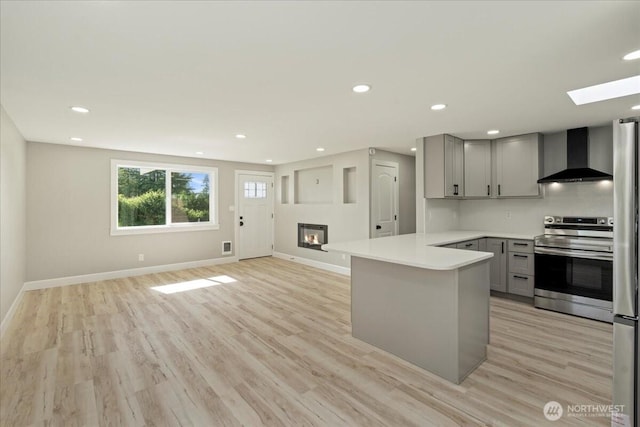 12102 19th Ct E, Edgewood, WA 98372 - kitchen featuring wall chimney exhaust hood, gray cabinetry, stainless steel appliances, a skylight, and a peninsula