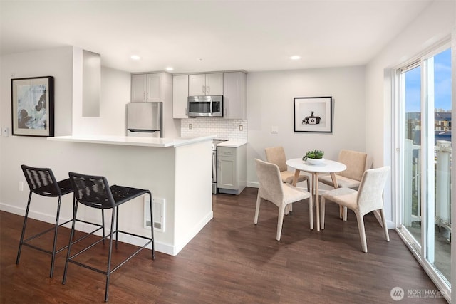 3318 30th Ave SW Unit A502, Seattle, WA 98126 - kitchen featuring stainless steel appliances, dark wood-type flooring, a breakfast bar area, light countertops, and backsplash