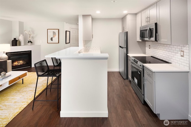 3318 30th Ave SW Unit A502, Seattle, WA 98126 - kitchen featuring appliances with stainless steel finishes, a peninsula, a kitchen bar, a glass covered fireplace, and dark wood finished floors