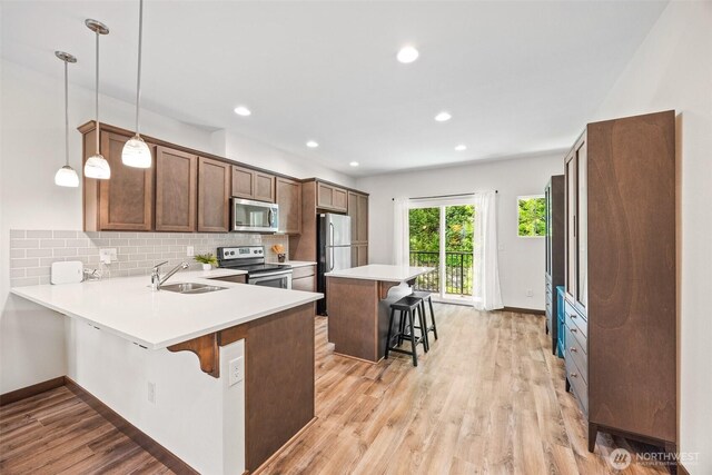 7165 27th Ave SW, Seattle, WA 98106 - kitchen featuring appliances with stainless steel finishes, a breakfast bar, a sink, tasteful backsplash, and light wood-style flooring