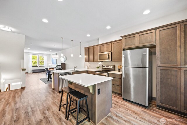 7165 27th Ave SW, Seattle, WA 98106 - kitchen with stainless steel appliances, a sink, a peninsula, light wood-type flooring, and backsplash