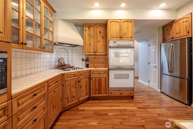 10303 Ski Hill Dr, Leavenworth, WA 98826 - kitchen featuring white appliances, custom range hood, tile counters, light wood-style floors, and tasteful backsplash