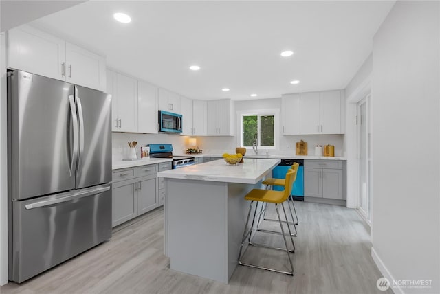5310 26th Ave S, Seattle, WA 98108 - kitchen featuring appliances with stainless steel finishes, light wood finished floors, a kitchen breakfast bar, a kitchen island, and recessed lighting