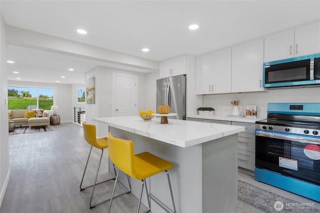 5310 26th Ave S, Seattle, WA 98108 - kitchen with appliances with stainless steel finishes, a center island, light wood-style flooring, light stone countertops, and a breakfast bar area