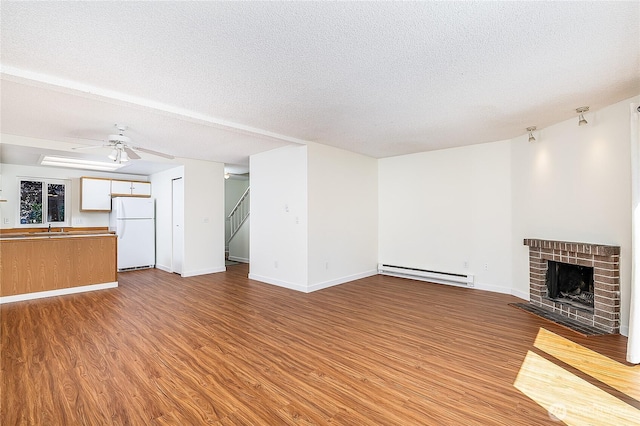 8823 Holly Dr Unit H207, Everett, WA 98208 - unfurnished living room featuring a baseboard radiator, light wood-style flooring, a textured ceiling, a fireplace, and ceiling fan
