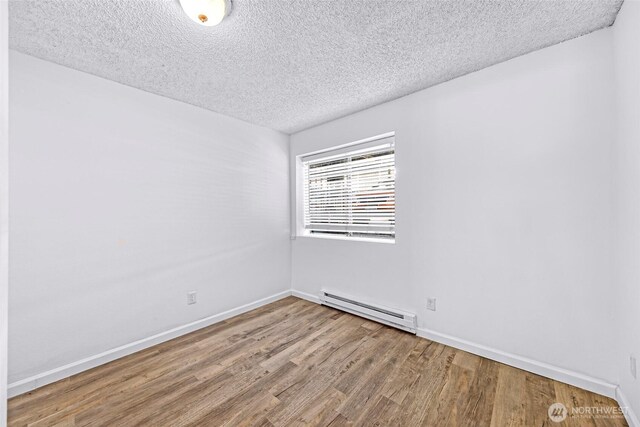 1338 Orleans St, Bellingham, WA 98229 - empty room featuring a baseboard heating unit, a textured ceiling, wood finished floors, and baseboards