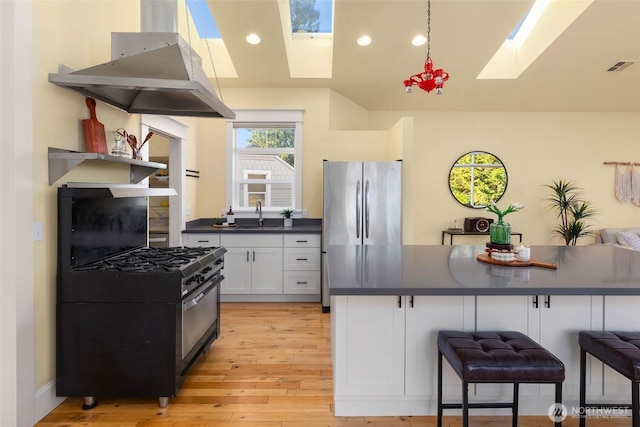 11744 NE Sand Point Way, Seattle, WA 98125 - kitchen with a skylight, wall chimney exhaust hood, gas stove, dark countertops, and light wood-type flooring
