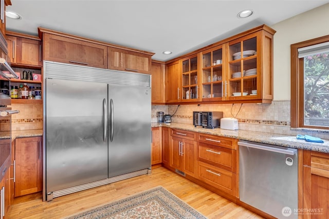 6490 NE Monte Vista Dr, Bainbridge Island, WA 98110 - kitchen featuring appliances with stainless steel finishes, brown cabinets, light wood-style floors, light stone counters, and decorative backsplash