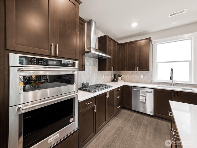 8310 115th Pl SE Unit 3, Newcastle, WA 98056 - kitchen featuring stainless steel appliances, wall chimney range hood, a sink, wood finished floors, and dark brown cabinetry