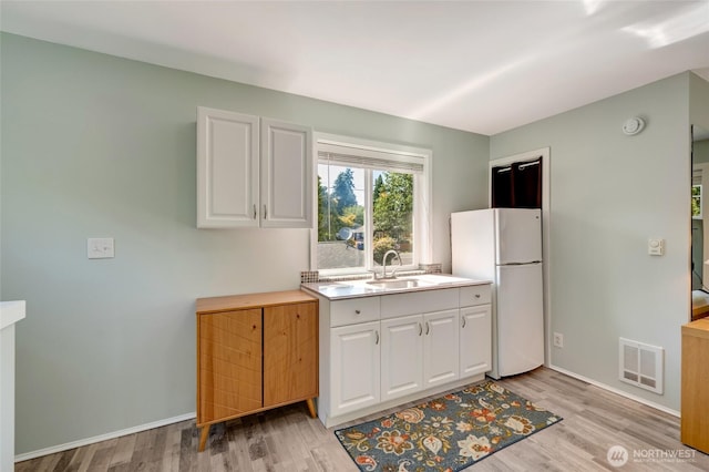 18008 Ashworth Ave N, Shoreline, WA 98133 - kitchen with freestanding refrigerator, a sink, white cabinetry, light countertops, and light wood-type flooring