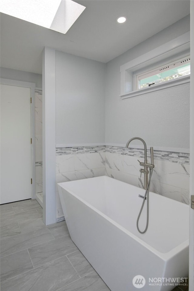 393 Canal Dr SE, Ocean Shores, WA 98569 - bathroom featuring tile walls, a freestanding tub, recessed lighting, a skylight, and wainscoting