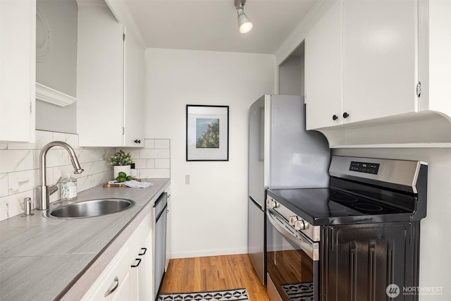 530 W Olympic Pl Unit 406, Seattle, WA 98119 - kitchen featuring appliances with stainless steel finishes, a sink, light wood-style flooring, white cabinetry, and tasteful backsplash