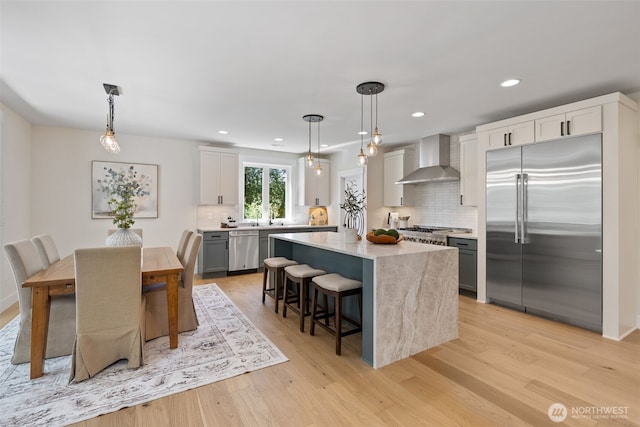 15001 NE 8th St, Bellevue, WA 98007 - kitchen with appliances with stainless steel finishes, wall chimney range hood, decorative backsplash, light wood-style floors, and a kitchen bar