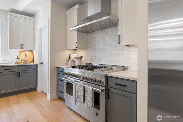 15001 NE 8th St, Bellevue, WA 98007 - kitchen featuring appliances with stainless steel finishes, wall chimney range hood, gray cabinetry, decorative backsplash, and light wood-style flooring