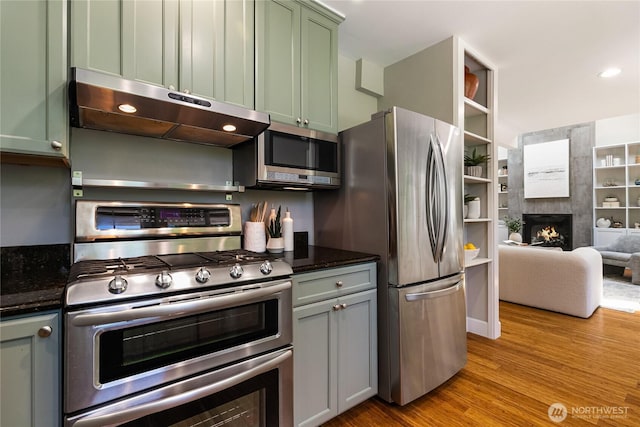 761 Chuckanut Dr, Bellingham, WA 98229 - kitchen with appliances with stainless steel finishes, green cabinets, under cabinet range hood, a tile fireplace, and wood finished floors