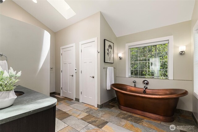 761 Chuckanut Dr, Bellingham, WA 98229 - bathroom with lofted ceiling, a soaking tub, stone tile floors, baseboards, and a skylight