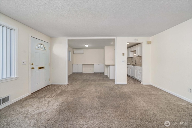 330 7th Pl SE Unit 4, Puyallup, WA 98372 - unfurnished living room with carpet floors, a wall unit AC, a sink, baseboards, and a textured ceiling