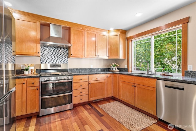 3276 Spyglass Dr, Bellingham, WA 98226 - kitchen featuring wall chimney exhaust hood, stainless steel appliances, a sink, light wood-type flooring, and dark stone counters