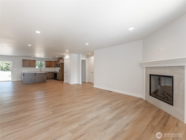 10 Salmon Dr, Wenatchee, WA 98801 - unfurnished living room featuring light wood finished floors, a tiled fireplace, recessed lighting, baseboards, and a sink