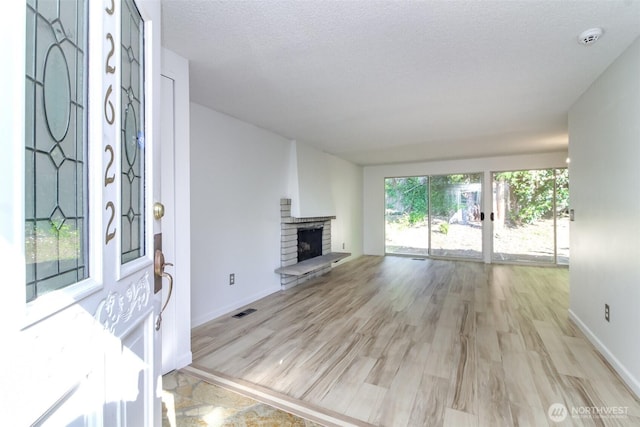 32622 39th Ave SW, Federal Way, WA 98023 - unfurnished living room featuring light wood-type flooring, a fireplace with raised hearth, baseboards, and a textured ceiling