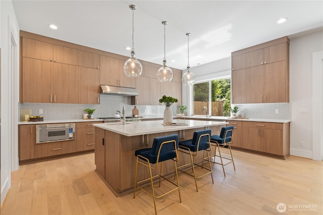 14511 SE 21st Pl, Bellevue, WA 98007 - kitchen featuring light wood-style floors, backsplash, a kitchen breakfast bar, an island with sink, and light countertops