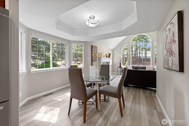 6579 Gleneagle Ave SW, Port Orchard, WA 98367 - dining space with light wood-type flooring, baseboards, a raised ceiling, a fireplace, and crown molding