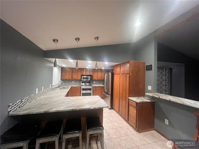 319 N Grape Dr, Moses Lake, WA 98837 - kitchen with appliances with stainless steel finishes, vaulted ceiling, brown cabinets, a peninsula, and decorative backsplash