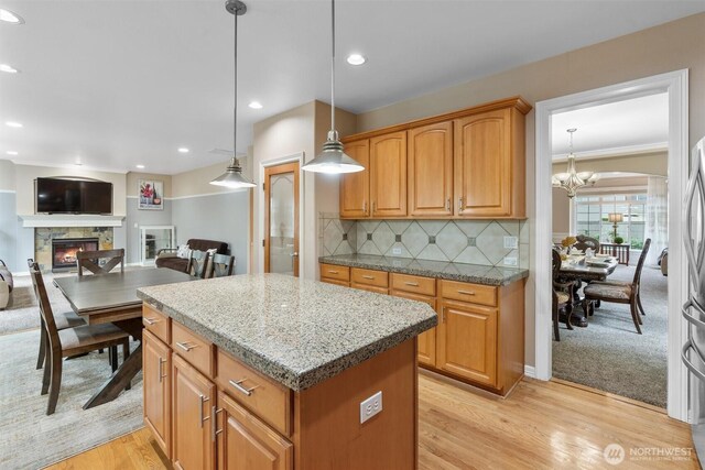 13327 SE 279th Pl, Kent, WA 98042 - kitchen featuring a kitchen island, a stone fireplace, a chandelier, light wood-style flooring, and decorative backsplash