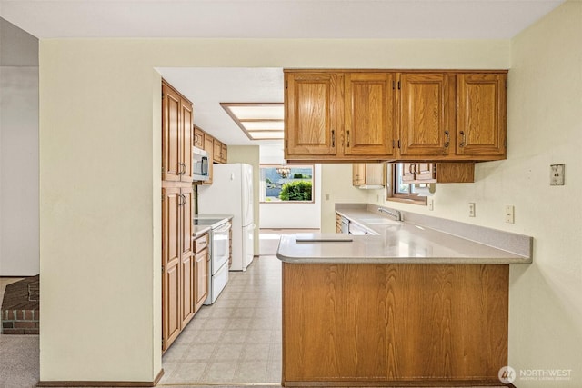 6410 151st Ave E, Sumner, WA 98390 - kitchen featuring white appliances, light flooring, a peninsula, a sink, and brown cabinetry