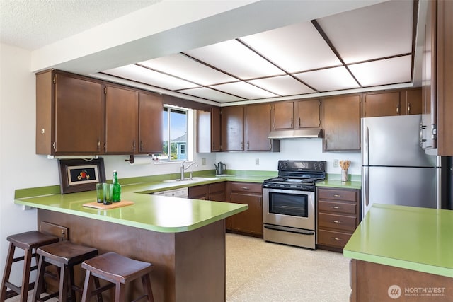 5228 56th Ave S, Seattle, WA 98118 - kitchen with appliances with stainless steel finishes, under cabinet range hood, a peninsula, a sink, and light countertops