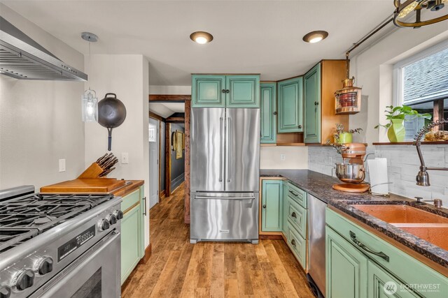 1811 Bay St, Port Orchard, WA 98366 - kitchen featuring stainless steel appliances, wall chimney exhaust hood, green cabinetry, light wood-type flooring, and backsplash