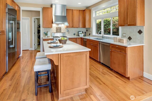 412 15th Ave, Kirkland, WA 98033 - kitchen featuring wall chimney range hood, built in appliances, a sink, light wood-style floors, and a kitchen breakfast bar