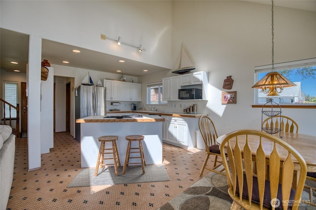 580 Mt Olympus Ave SE, Ocean Shores, WA 98569 - kitchen featuring black microwave, a towering ceiling, white cabinets, wood counters, and a kitchen island