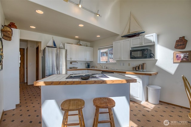 580 Mt Olympus Ave SE, Ocean Shores, WA 98569 - kitchen with freestanding refrigerator, cooktop, a breakfast bar area, white cabinets, and recessed lighting