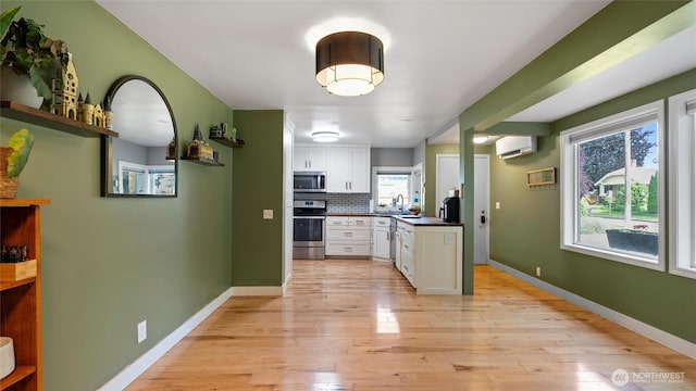 1109 University St, Walla Walla, WA 99362 - kitchen with appliances with stainless steel finishes, a wall mounted AC, white cabinetry, light wood-style flooring, and a sink