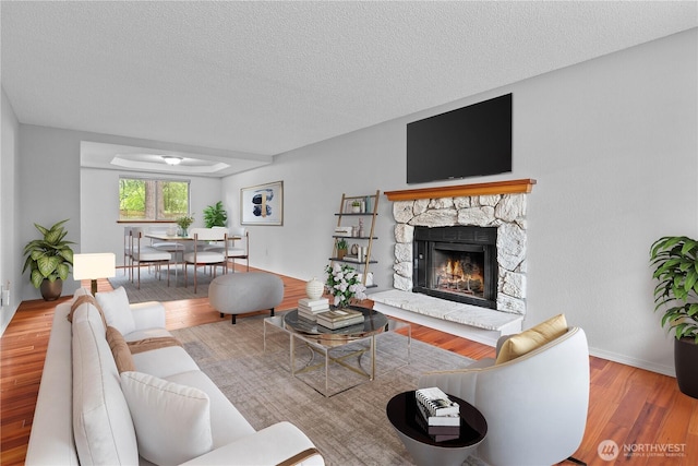 18802 10th Avenue Ct E, Tacoma, WA 98387 - living room featuring wood finished floors, a textured ceiling, a stone fireplace, and baseboards