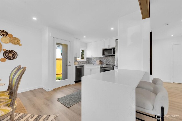 8042 19th Ave NW, Seattle, WA 98117 - kitchen featuring appliances with stainless steel finishes, backsplash, white cabinetry, light wood-style floors, and light countertops