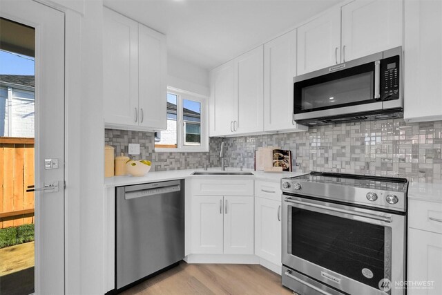 8042 19th Ave NW, Seattle, WA 98117 - kitchen with stainless steel appliances, a sink, light countertops, white cabinetry, and decorative backsplash