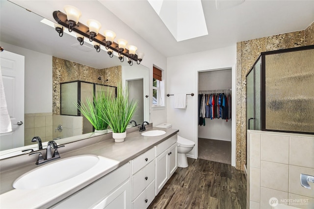 3534 SW Monroe St, Seattle, WA 98126 - bathroom with wood finished floors, double vanity, a stall shower, a skylight, and toilet