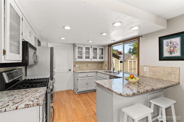 4404 29th Ave SE, Lacey, WA 98503 - kitchen with stainless steel range with gas cooktop, a peninsula, decorative backsplash, light wood-type flooring, and black microwave