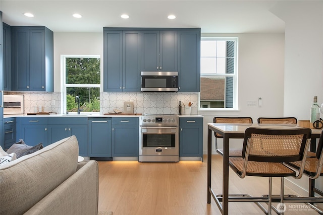 3639 34th Ave W Unit B, Seattle, WA 98199 - kitchen with stainless steel appliances, a sink, light wood-style flooring, blue cabinetry, and recessed lighting